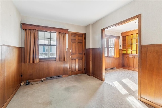 carpeted entrance foyer with a baseboard radiator and wooden walls