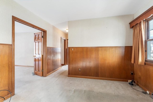 empty room with a wealth of natural light, light colored carpet, and wood walls