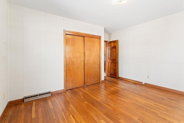 unfurnished bedroom featuring a baseboard heating unit, a closet, and light wood-type flooring