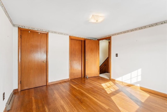 unfurnished bedroom featuring hardwood / wood-style floors, a closet, and a baseboard heating unit