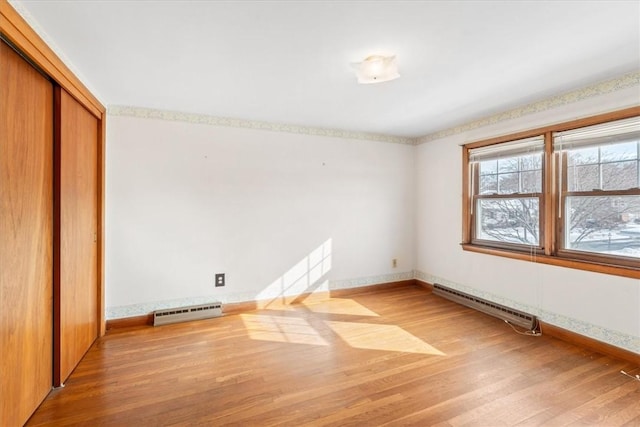 unfurnished bedroom featuring a baseboard radiator, hardwood / wood-style floors, and a closet