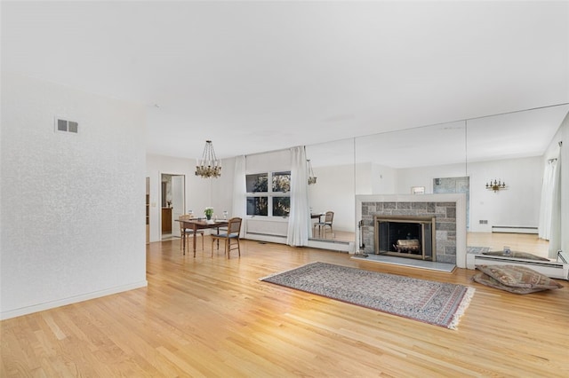 living room featuring baseboard heating, hardwood / wood-style floors, an inviting chandelier, and a stone fireplace