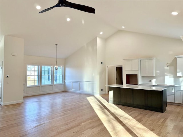 kitchen featuring white cabinetry, light hardwood / wood-style flooring, ceiling fan with notable chandelier, hanging light fixtures, and a kitchen island