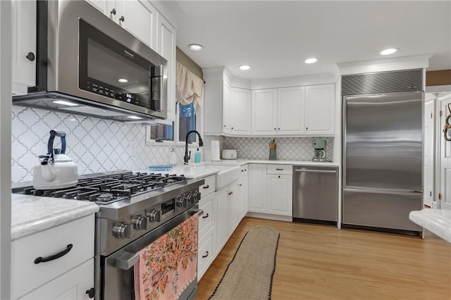 kitchen featuring sink, white cabinets, light wood-type flooring, tasteful backsplash, and premium appliances