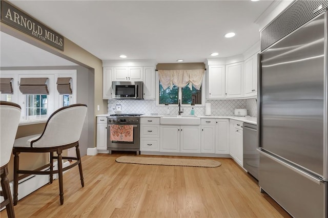 kitchen featuring light hardwood / wood-style flooring, premium appliances, backsplash, white cabinets, and sink