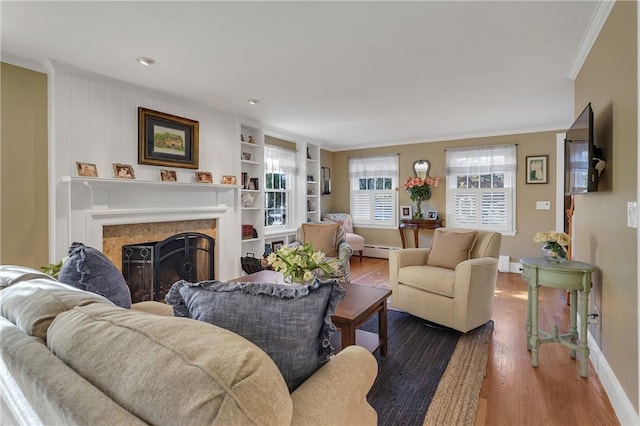 living room featuring a tile fireplace, crown molding, hardwood / wood-style flooring, a baseboard radiator, and built in shelves