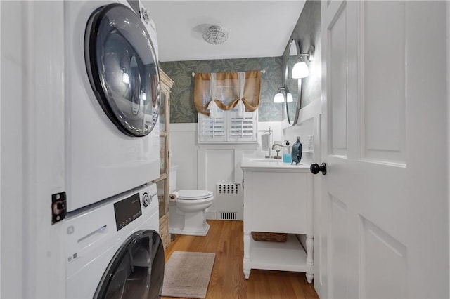 bathroom featuring stacked washing maching and dryer, hardwood / wood-style flooring, radiator, toilet, and vanity