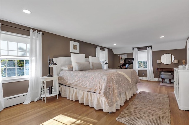 bedroom with lofted ceiling, a baseboard radiator, and light wood-type flooring