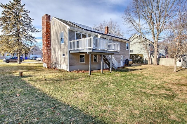 rear view of property with a wooden deck, solar panels, and a lawn