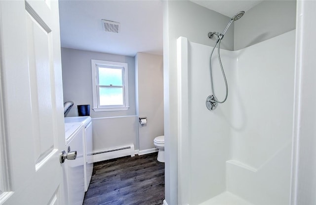 bathroom with a baseboard heating unit, a shower, washing machine and clothes dryer, and hardwood / wood-style flooring