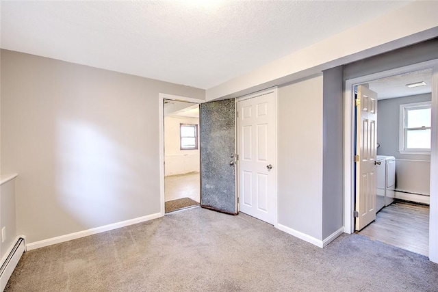 unfurnished bedroom with washing machine and dryer, multiple windows, a baseboard heating unit, and light carpet