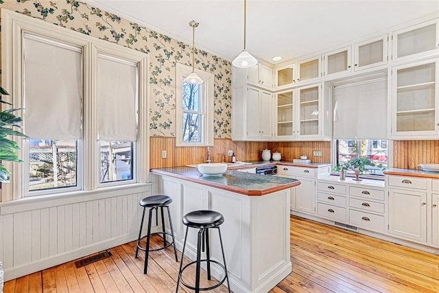 kitchen with kitchen peninsula, pendant lighting, light hardwood / wood-style floors, white cabinets, and a kitchen breakfast bar