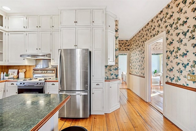 kitchen with white gas stove, white cabinetry, light hardwood / wood-style flooring, stainless steel refrigerator, and crown molding