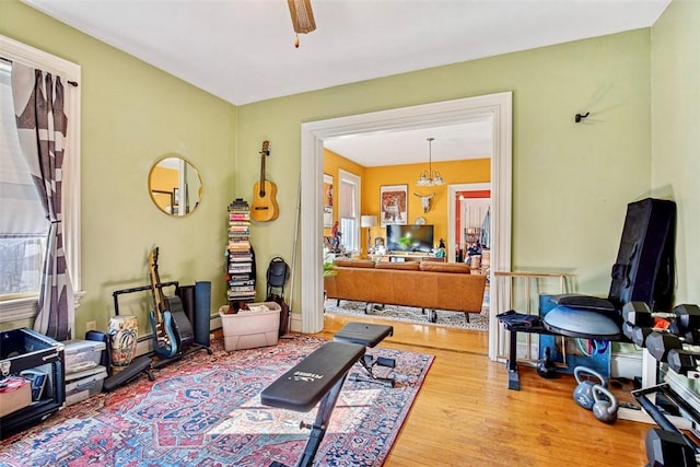 exercise area with ceiling fan with notable chandelier and hardwood / wood-style flooring