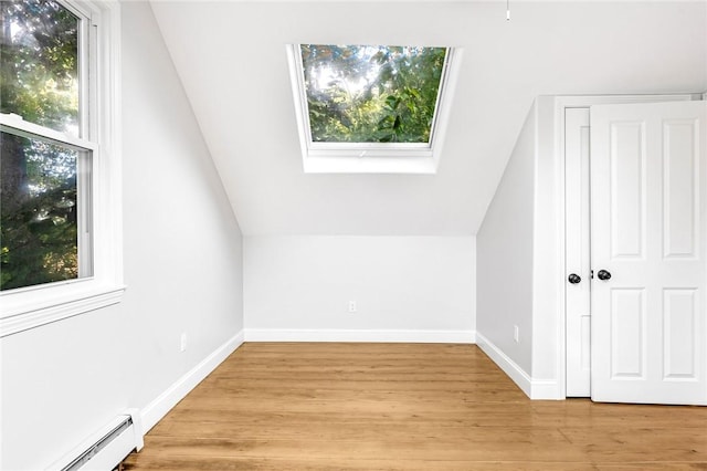 additional living space with light wood-type flooring, vaulted ceiling, and a baseboard heating unit