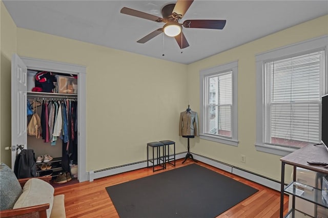 workout area featuring a baseboard heating unit, light wood-type flooring, and ceiling fan