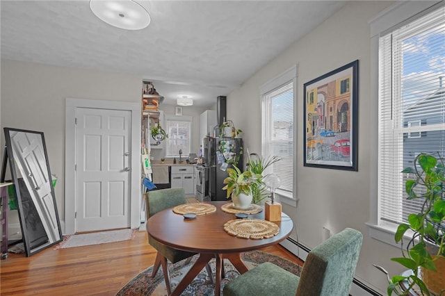 dining area featuring light hardwood / wood-style floors, a baseboard heating unit, and a healthy amount of sunlight