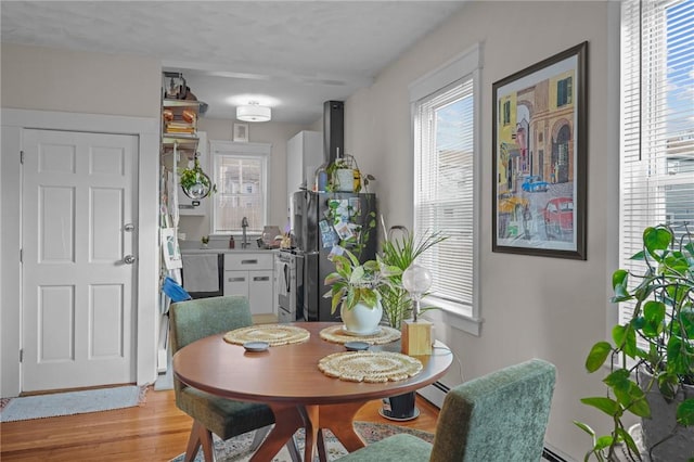 dining area featuring sink, baseboard heating, and light hardwood / wood-style flooring