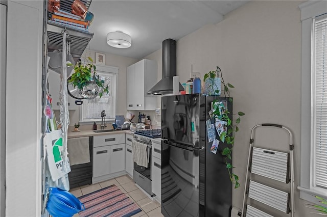 kitchen featuring sink, white cabinets, wall chimney exhaust hood, stainless steel gas stove, and black refrigerator