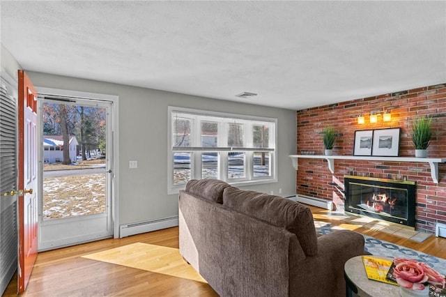 living room featuring a baseboard heating unit, a wealth of natural light, a fireplace, and light hardwood / wood-style floors