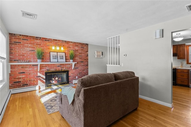 living room featuring light hardwood / wood-style flooring, a fireplace, brick wall, and baseboard heating