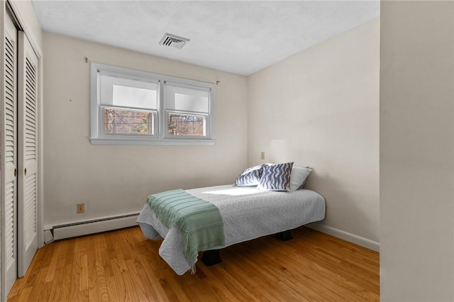 bedroom featuring light wood-type flooring, a closet, and a baseboard heating unit