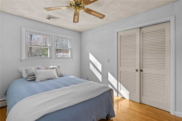 bedroom featuring a baseboard radiator, light hardwood / wood-style flooring, ceiling fan, and a closet