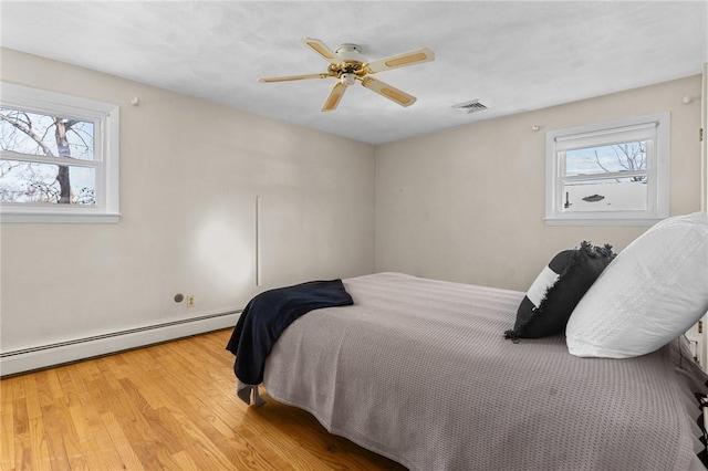 bedroom with multiple windows, a baseboard radiator, light hardwood / wood-style floors, and ceiling fan