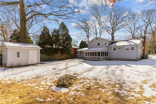 snow covered rear of property with a sunroom, central AC, and a storage unit