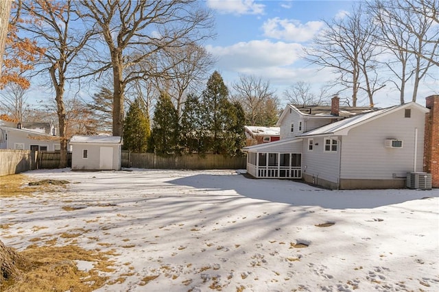 yard layered in snow featuring a shed, a sunroom, and central air condition unit