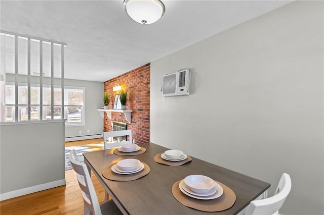 dining room featuring a baseboard radiator, a wall mounted AC, light hardwood / wood-style floors, and a brick fireplace