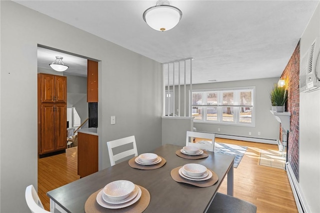 dining space featuring a brick fireplace, light wood-type flooring, and baseboard heating