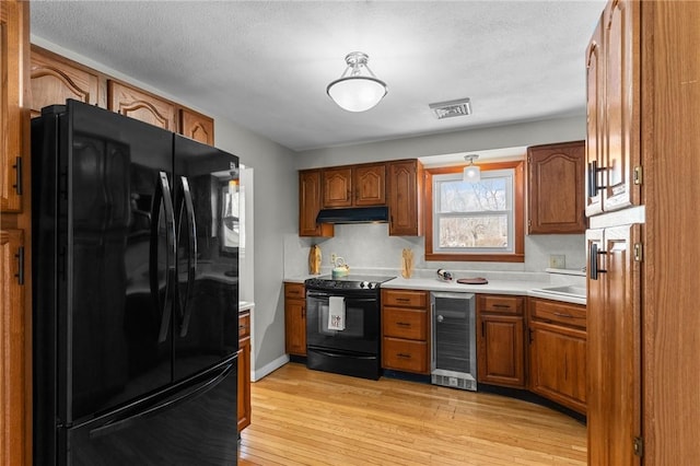 kitchen with wine cooler, black appliances, a textured ceiling, and light wood-type flooring