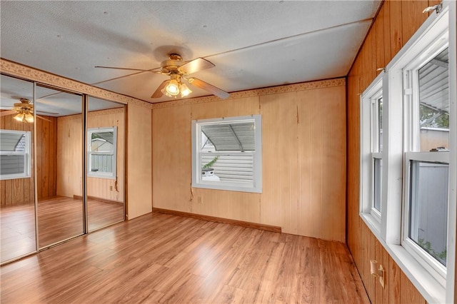 unfurnished bedroom with wood walls, a closet, ceiling fan, and light hardwood / wood-style flooring