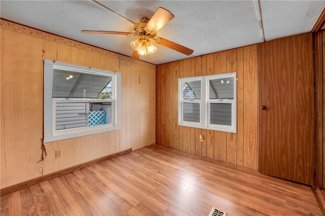 unfurnished room with wood walls, light wood-type flooring, and ceiling fan