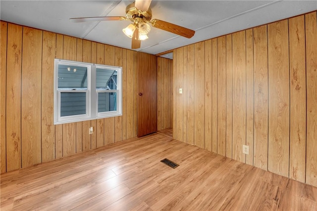 spare room featuring ceiling fan, light hardwood / wood-style flooring, and wooden walls