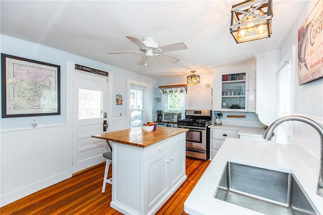 kitchen with sink, stainless steel range with gas cooktop, white cabinetry, hanging light fixtures, and a kitchen island