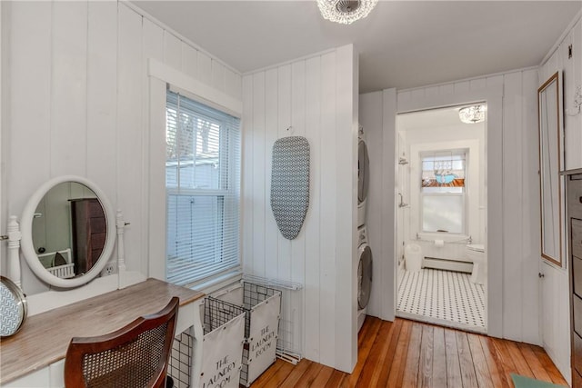 laundry area with stacked washer and dryer, wood walls, light wood-type flooring, and an inviting chandelier