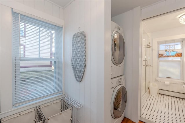 laundry area featuring wood walls, baseboard heating, and stacked washer / dryer