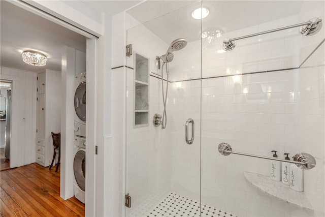 bathroom featuring stacked washer and clothes dryer, hardwood / wood-style floors, and a shower with shower door