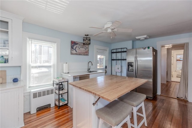 kitchen featuring stainless steel fridge with ice dispenser, a breakfast bar, white cabinetry, radiator heating unit, and sink