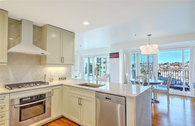 kitchen featuring stainless steel appliances, kitchen peninsula, wall chimney exhaust hood, sink, and backsplash