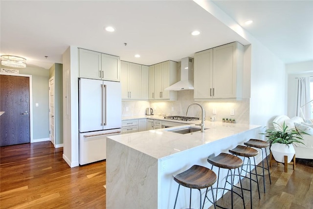 kitchen featuring sink, wall chimney exhaust hood, high end white fridge, light hardwood / wood-style floors, and a breakfast bar area