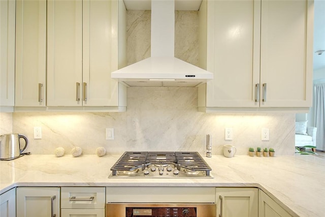 kitchen with tasteful backsplash, light stone counters, stainless steel gas cooktop, and wall chimney exhaust hood