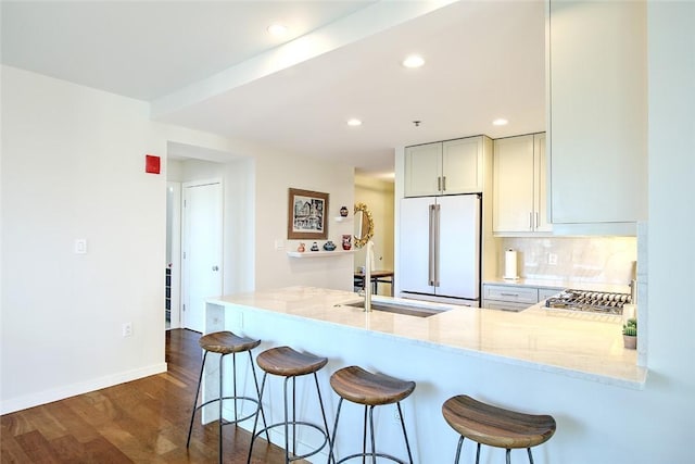 kitchen featuring sink, light stone counters, high quality fridge, kitchen peninsula, and a breakfast bar area