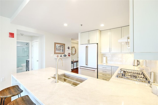 kitchen with white cabinets, high end white fridge, kitchen peninsula, stainless steel gas stovetop, and sink