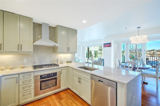 kitchen with appliances with stainless steel finishes, kitchen peninsula, pendant lighting, wall chimney exhaust hood, and sink