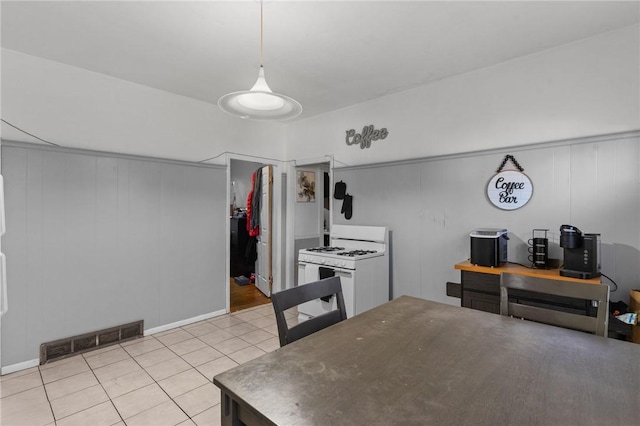 kitchen featuring light tile patterned floors, hanging light fixtures, wooden walls, and white gas range oven