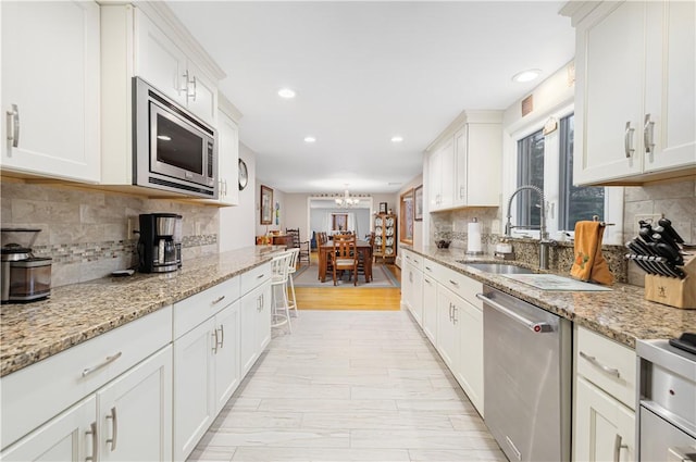 kitchen with stainless steel appliances, sink, white cabinetry, decorative backsplash, and light stone countertops