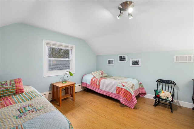 bedroom with a baseboard heating unit, vaulted ceiling, and hardwood / wood-style floors